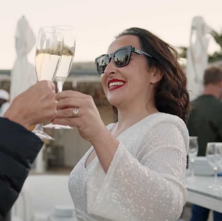 Woman in sunglasses clinking champagne glasses at outdoor celebration.