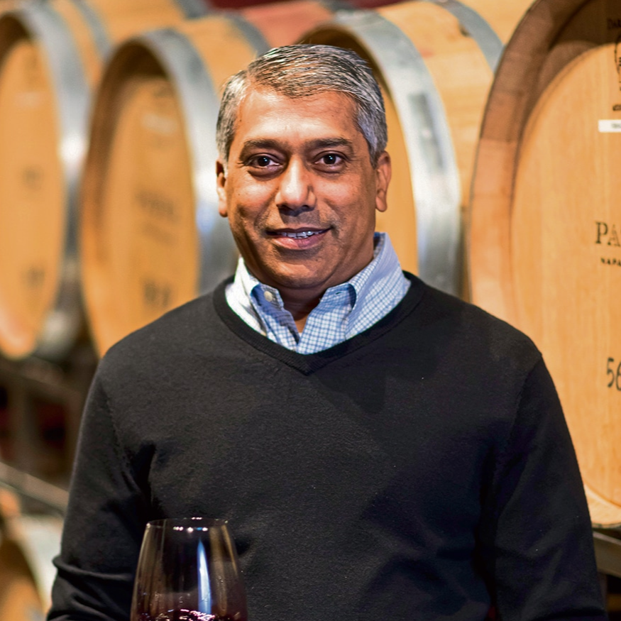 Raj Patel in a winery with wine barrels in the background.